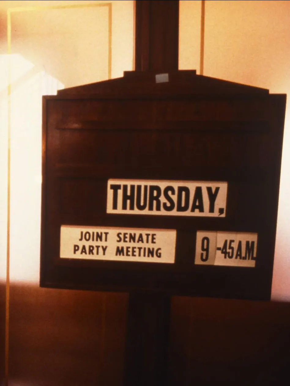Party meetings were a regular fixture in the Senate Opposition Party Room when parliament was sitting, 1988.
Photograph by Robert McFarlane, Department of the House of Representatives A wooden sign with the text 'Thursday, joint Senate party meeting, 9.45 a.m.' stands outside the door of a room with red carpet in Old Parliament House.
