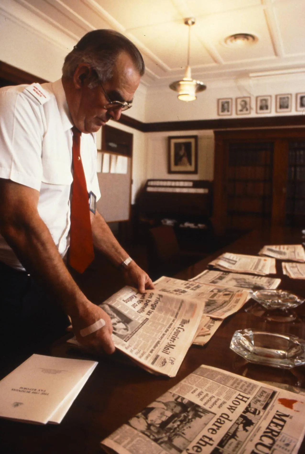 An attendant arranges the daily newspapers in the Senate Opposition Party Room, 1988.
Photograph by Robert McFarlane, Department of the House of Representatives A man wearing a white shirt and red tie arranges newspapers on a table in Old Parliament House.