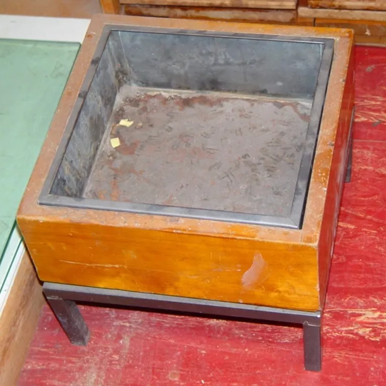 Wooden floor ashtray with a metal insert. A square wooden ashtray with a metal insert and sitting on a metal base with four small legs.