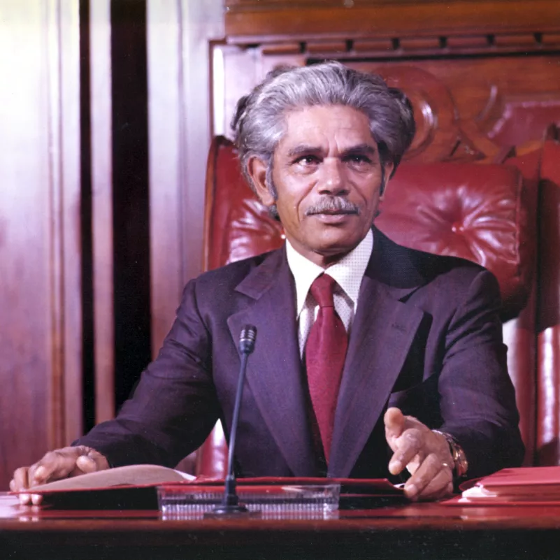 Neville Bonner AO. MoAD collection. Neville Bonner seated in the Senate chamber, wearing a suit and red tie.