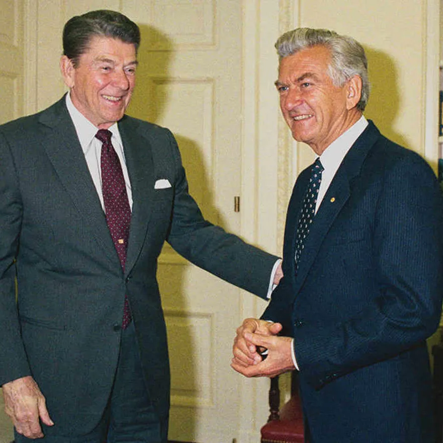 ‘Ron and Bob’ came to be fast friends, despite their differences. This photo was taken in 1986, on one of Hawke’s many more visits to the Reagan White House. Image: National Archives of Australia Ronald Reagan reaches an arm out to Bob Hawke, both smiling and wearing suits.