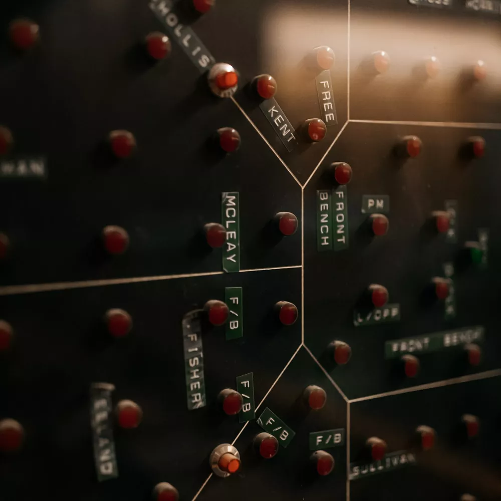 A close up of a layout of the House of Representatives Chamber with red lights representing each person in the chamber and black and black labels with names.