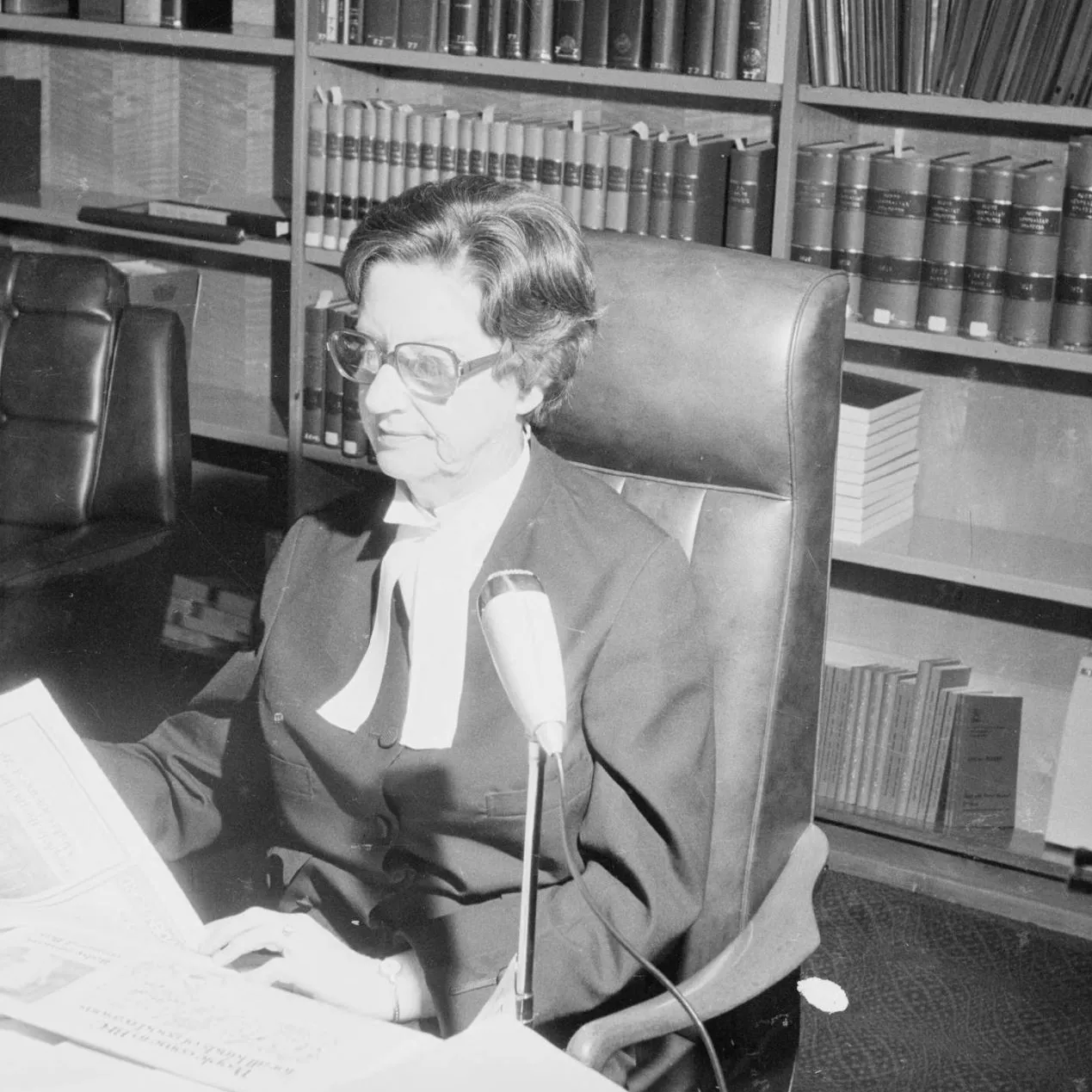 Dame Roma Mitchell, appointed Governor of South Australia in 1991, was the first woman to serve as an Australian state governor. As of 2018, every state has had at least one woman in its Government House.
Photograph National Library of Australia
A woman, Justice Roma Mitchell sits at a desk covered in papers, in front of a bookshelf filled with bound volumes.