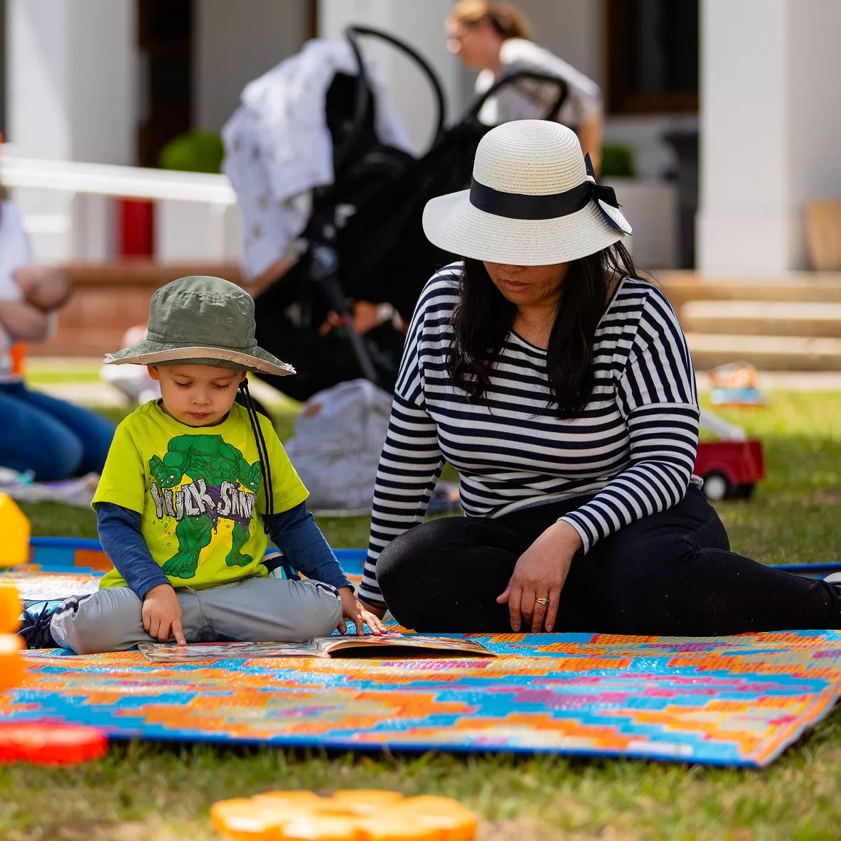 A child reading a book with their adult carer on a colourful mat on the lawn. A child reading a book with their adult carer on a colourful mat on the lawn.