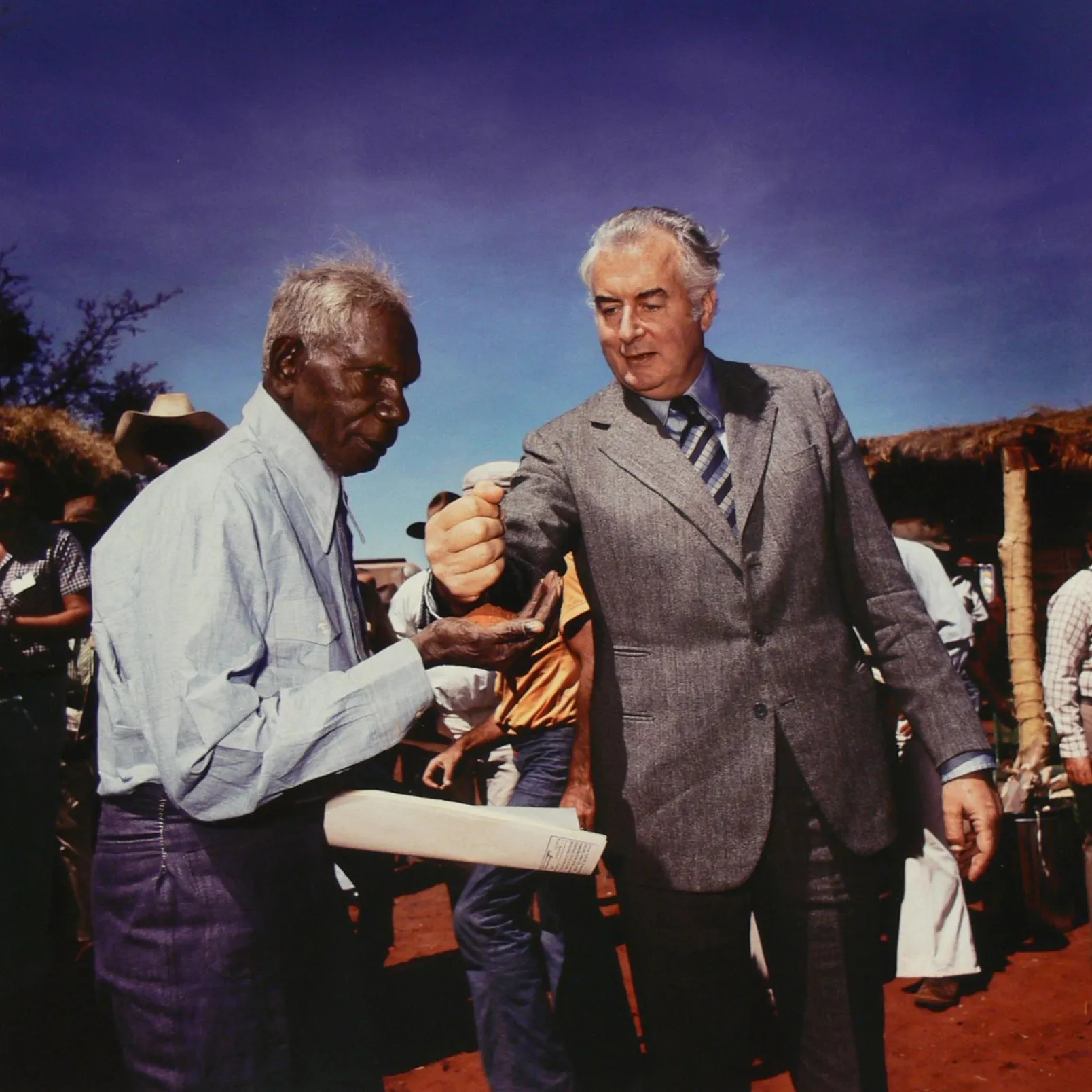 This photo of Gough Whitlam pouring earth through Vincent Lingiari’s hand has become an iconic image. It was taken by Mervyn Bishop on 16 August 1975. Museum of Australian Democracy Collection. Prime Minister Gough Whitlam pouring earth through Vincent Lingiari’s hand while people look on.