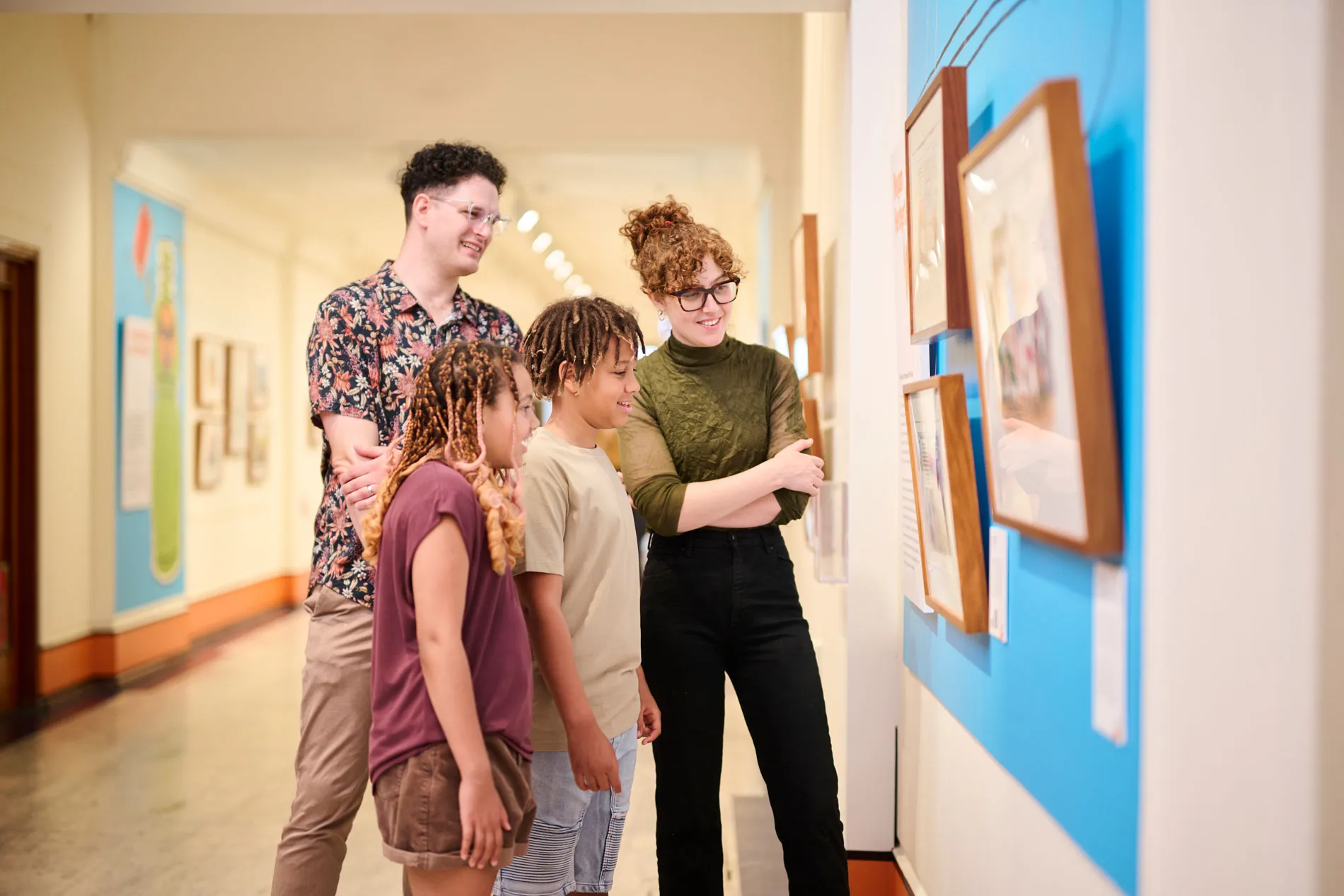 A smiling man, woman and two kids stand in a corridor at Old Parliament House looking at a political cartooning exhibition. A smiling man, woman and two kids stand in a corridor at Old Parliament House looking at a political cartooning exhibition.
