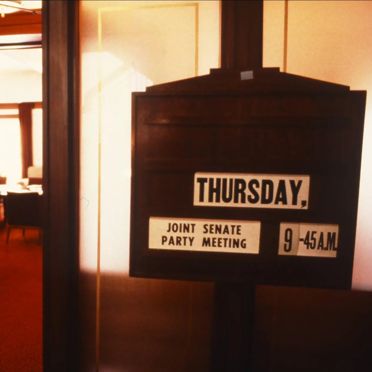 Party meetings were a regular fixture in the Senate Opposition Party Room when parliament was sitting, 1988.
Photograph by Robert McFarlane, Department of the House of Representatives A wooden sign with the text 'Thursday, joint Senate party meeting, 9.45 a.m.' stands outside the door of a room with red carpet in Old Parliament House.
