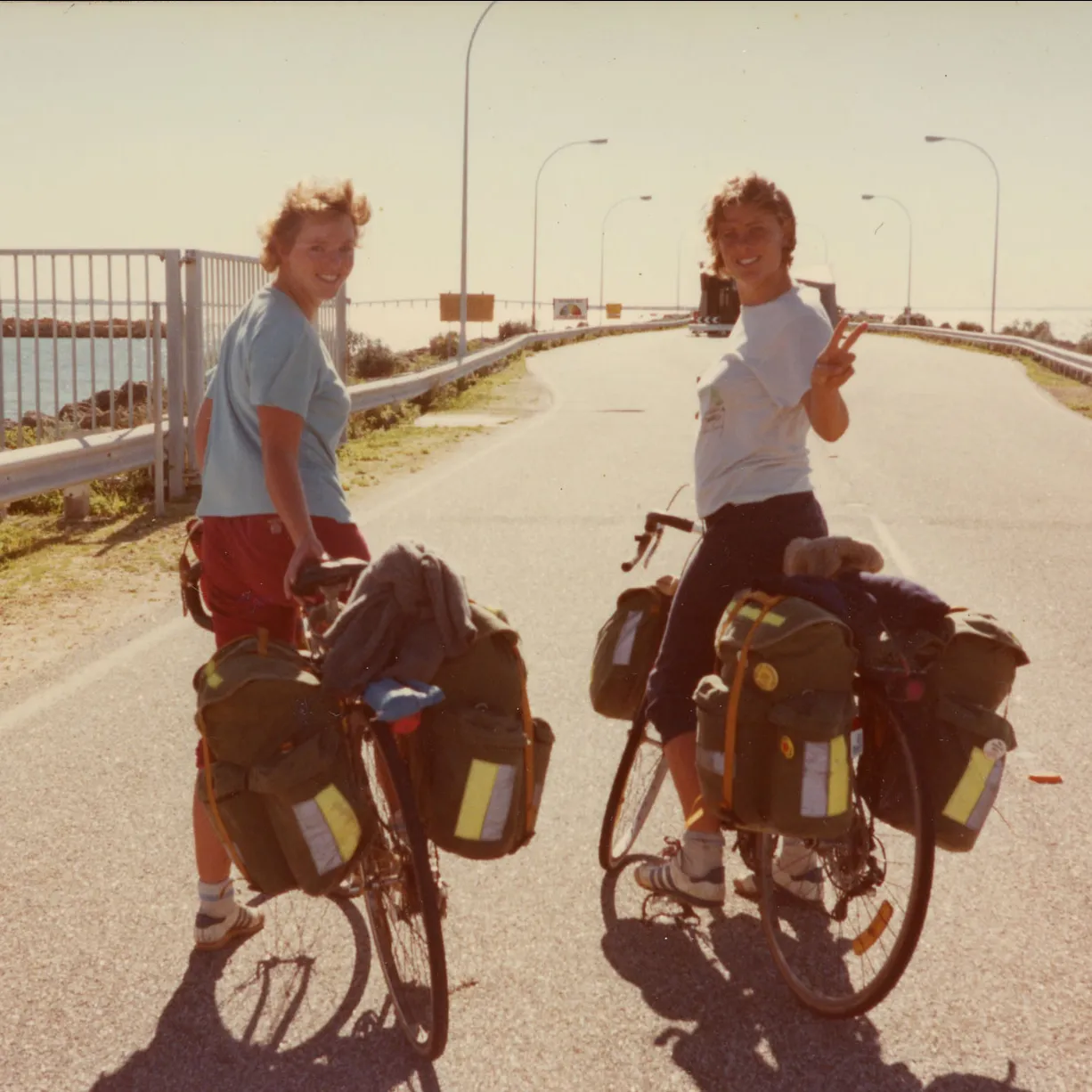 Two women on bikes on a road near the ocean.