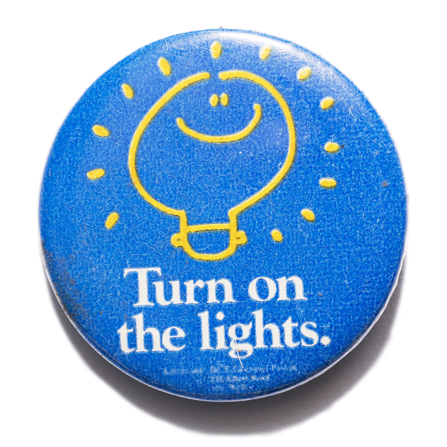 A blue badge with white text and a yellow lightbulb with a smiley face. Text reads, 'Turn on the lights'.