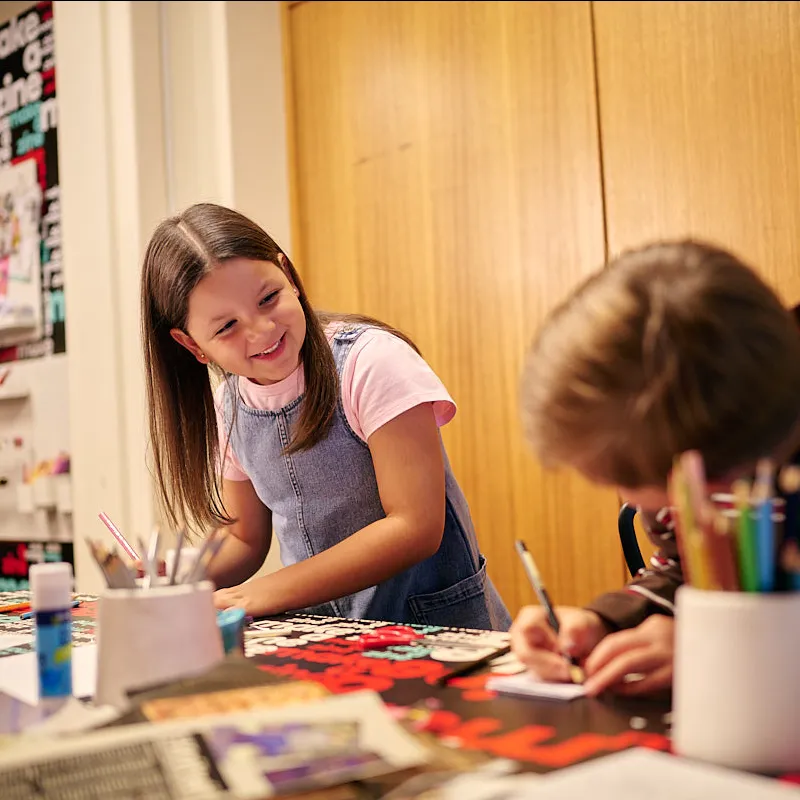 Two kids creating zines in the Zine Lounge, laughing with each other.