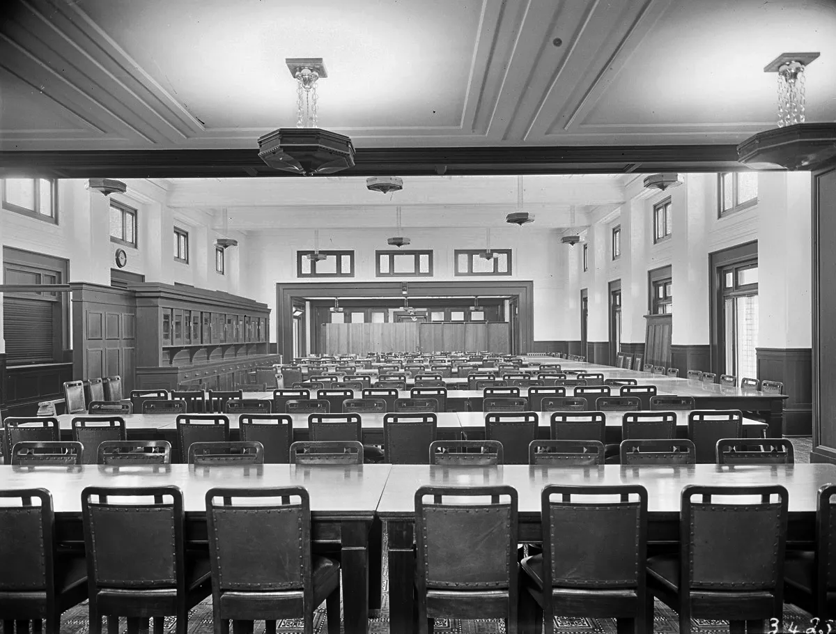 This black and white photograph looks along the length of the high-ceilinged Members’ Dining Room at Parliament House. Northern light floods in from windows and French doors on the right-hand wall. Rows of rectangular dining tables surrounded by hundreds of dining chairs span the width of the crowded room and on the left-hand wall is a timber servery. This black and white photograph looks along the length of the high-ceilinged Members’ Dining Room at Parliament House. Northern light floods in from windows and French doors on the right-hand wall. Rows of rectangular dining tables surrounded by hundreds of dining chairs span the width of the crowded room and on the left-hand wall is a timber servery.