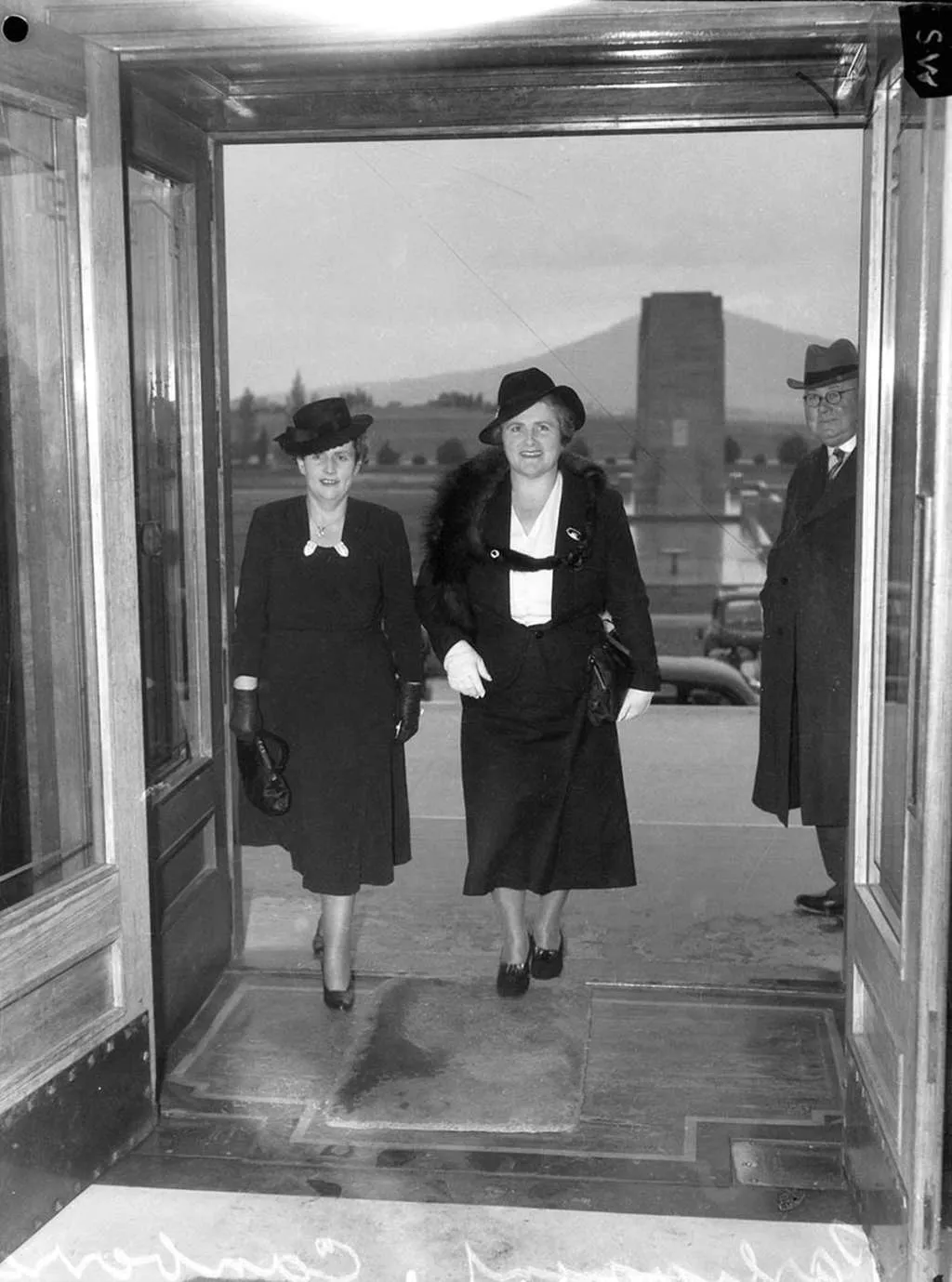 A black and white photo of Dorothy Tangney and Enid Lyons wearing dress suits and hats walking in through the front door of Old Parliament House. A black and white photo of Dorothy Tangney and Enid Lyons wearing dress suits and hats walking in through the front door of Old Parliament House.