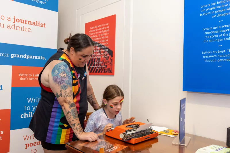 A child trying a typewriter while an adult watches on A child trying a typewriter while an adult watches on