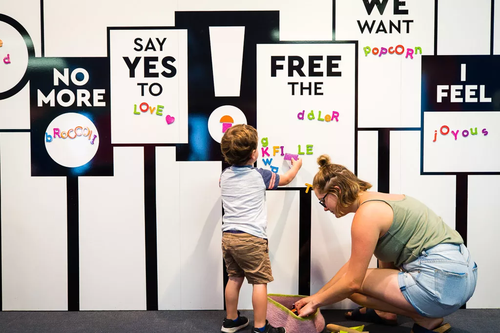 A small boy and his mother place magnets onto a wall with prompts such as 'say yes to love'. A small boy and his mother place magnets onto a wall with prompts such as 'say yes to love'.