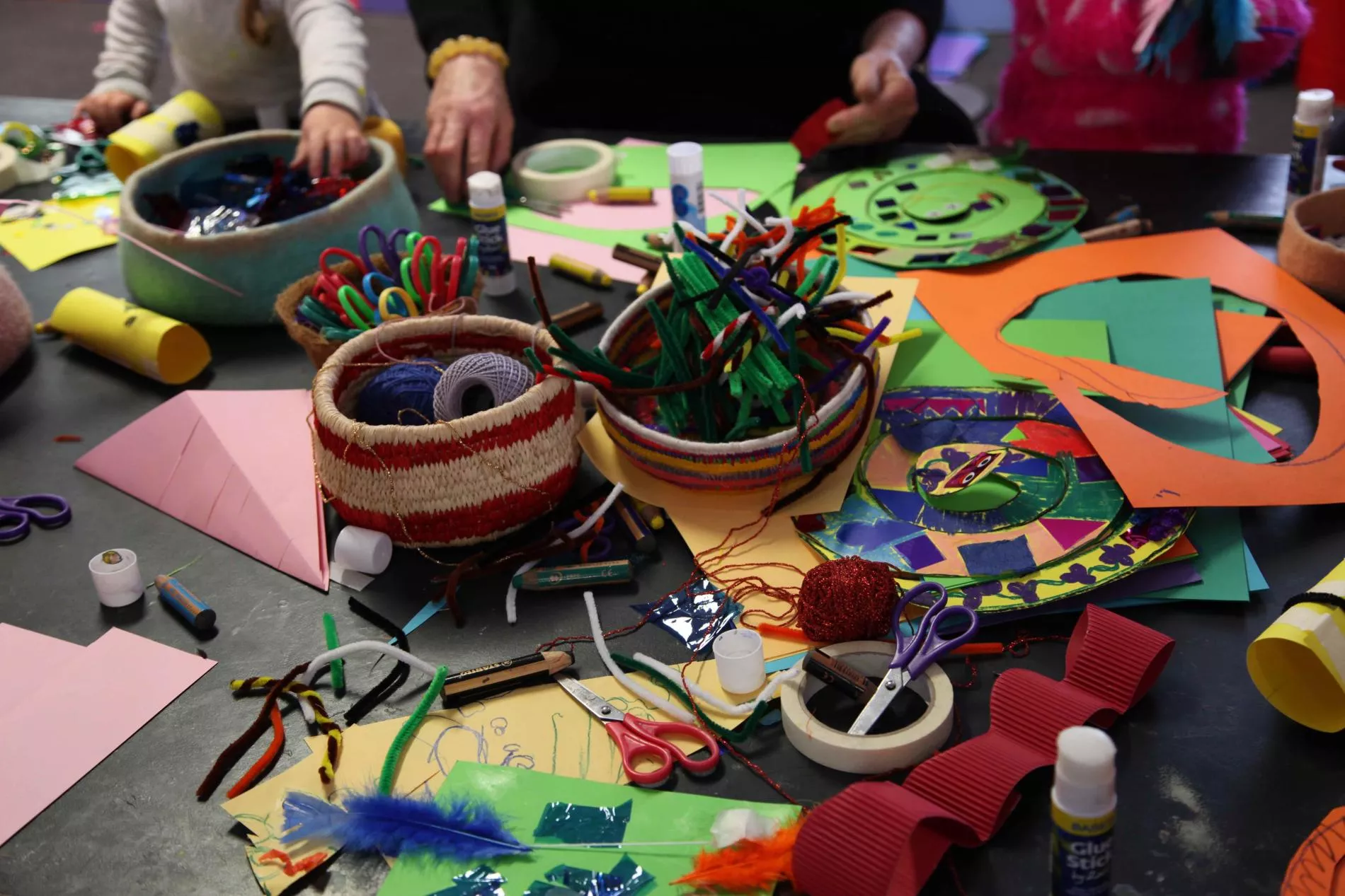 A table covered in coloured paper, feathers, scissors, glue, string and craft supplies. A table covered in coloured paper, feathers, scissors, glue, string and craft supplies.
