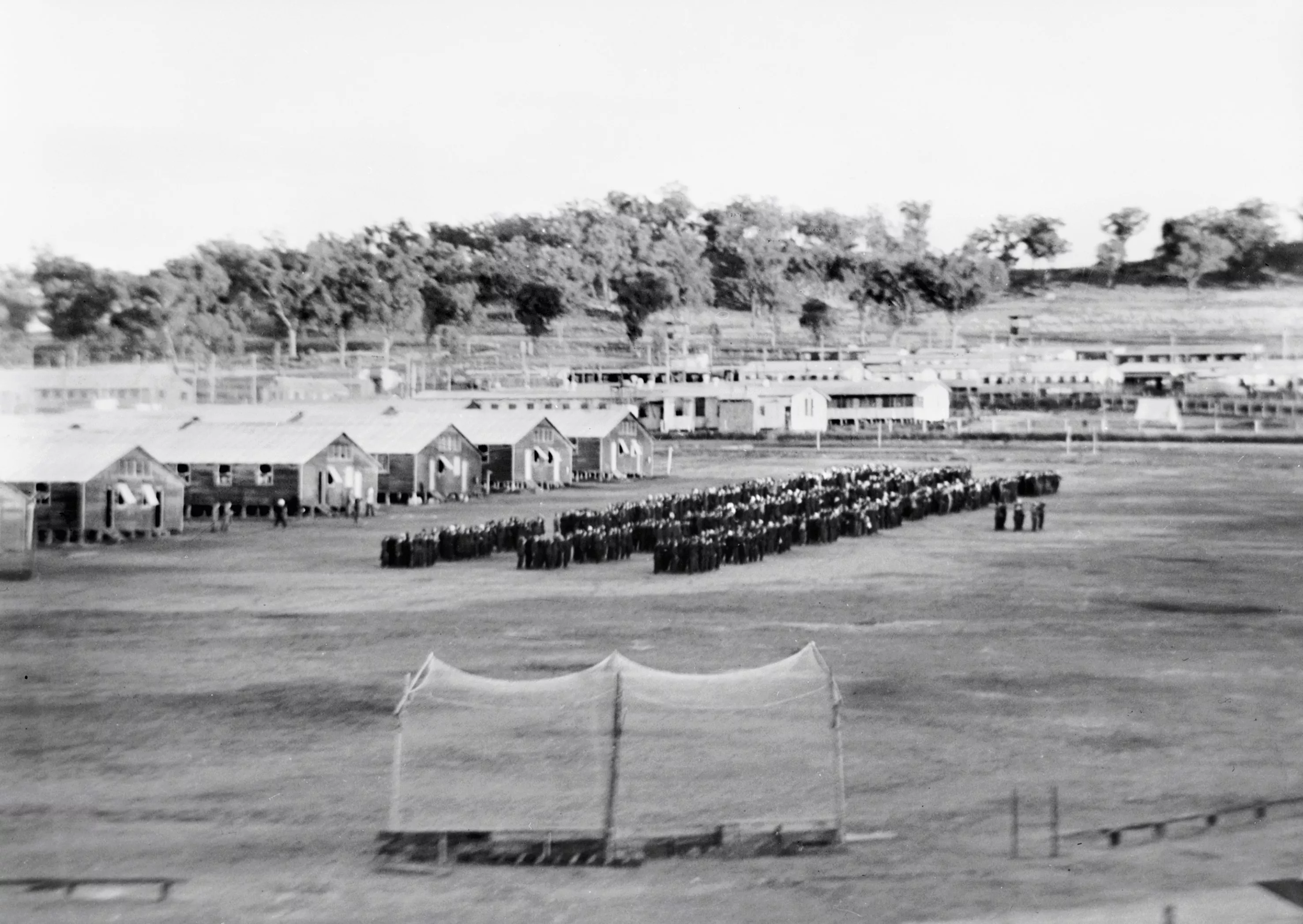 Lines of Japanese prisoners seen from far away, lined up in a ritualistic manner in front of many military huts inside an internment camp. Lines of Japanese prisoners seen from far away, lined up in a ritualistic manner in front of many military huts inside an internment camp.
