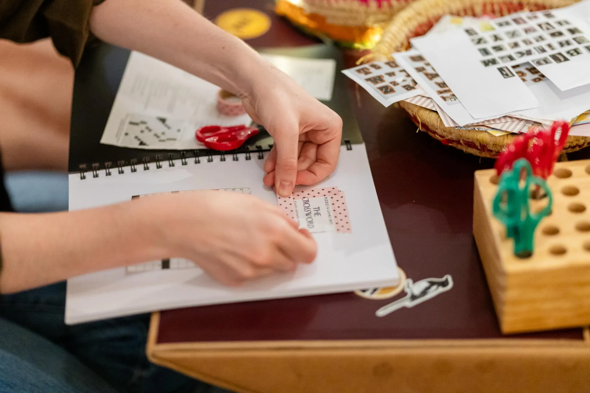 Hands work on a scrapbook at a desk filled with paper and scissors in Old Parliament House.